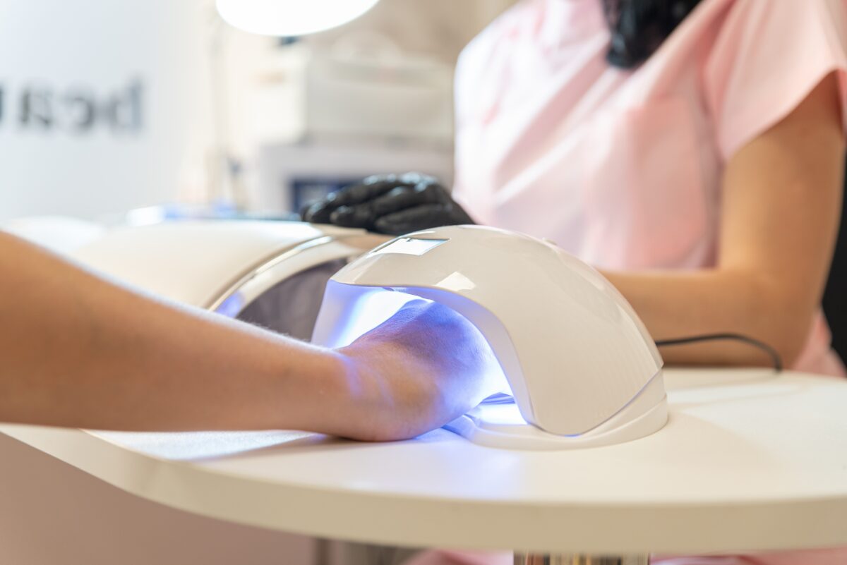 Woman holds fresh manicure in the UV LED nail lamp. Process of drying gel on nails, close up. Woman in beauty salon. Beauty and self care
