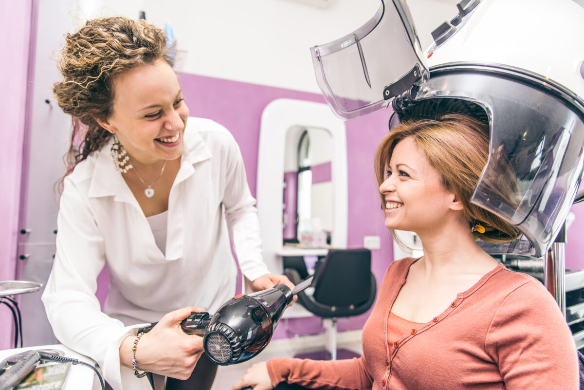 Beautician blow drying woman's hair after giving a new haircut - Hairdresser talking and smiling with her customer during a beauty hair treatment