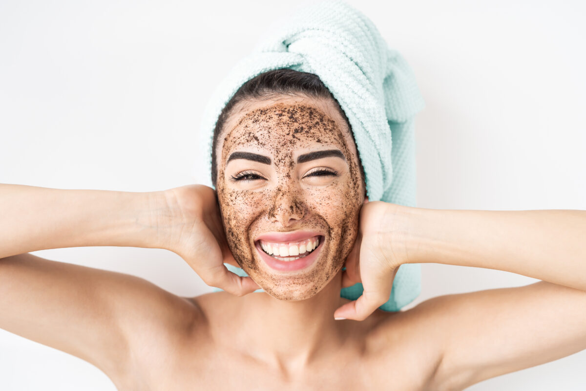 Young smiling woman applying coffee scrub mask on face - Happy girl having skin care spa day at home - Healthy alternative natural exfoliation treatment and people lifestyle concept