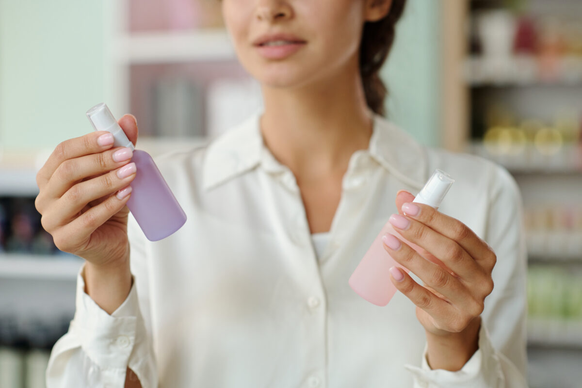 Hands of young shopper holding two plastic bottles polish removers with liquid nailcare products in nail salon while deciding which one to choose