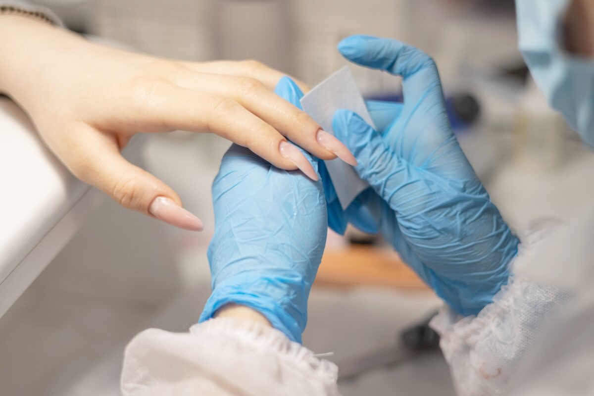 Removing the OPI Infinite Shine shade from the clients' nails in a nail salon by a professional nail technician