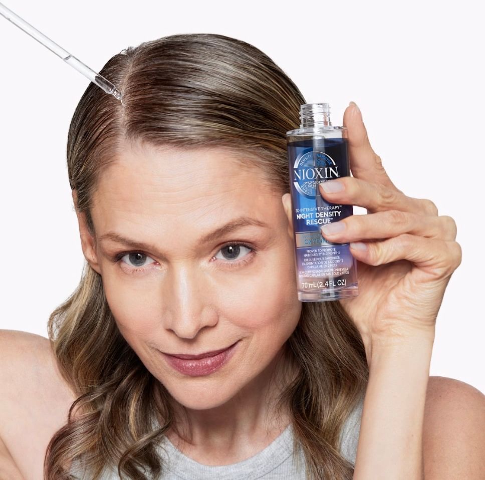 A beautiful woman is applying a Nioxin product to her hair