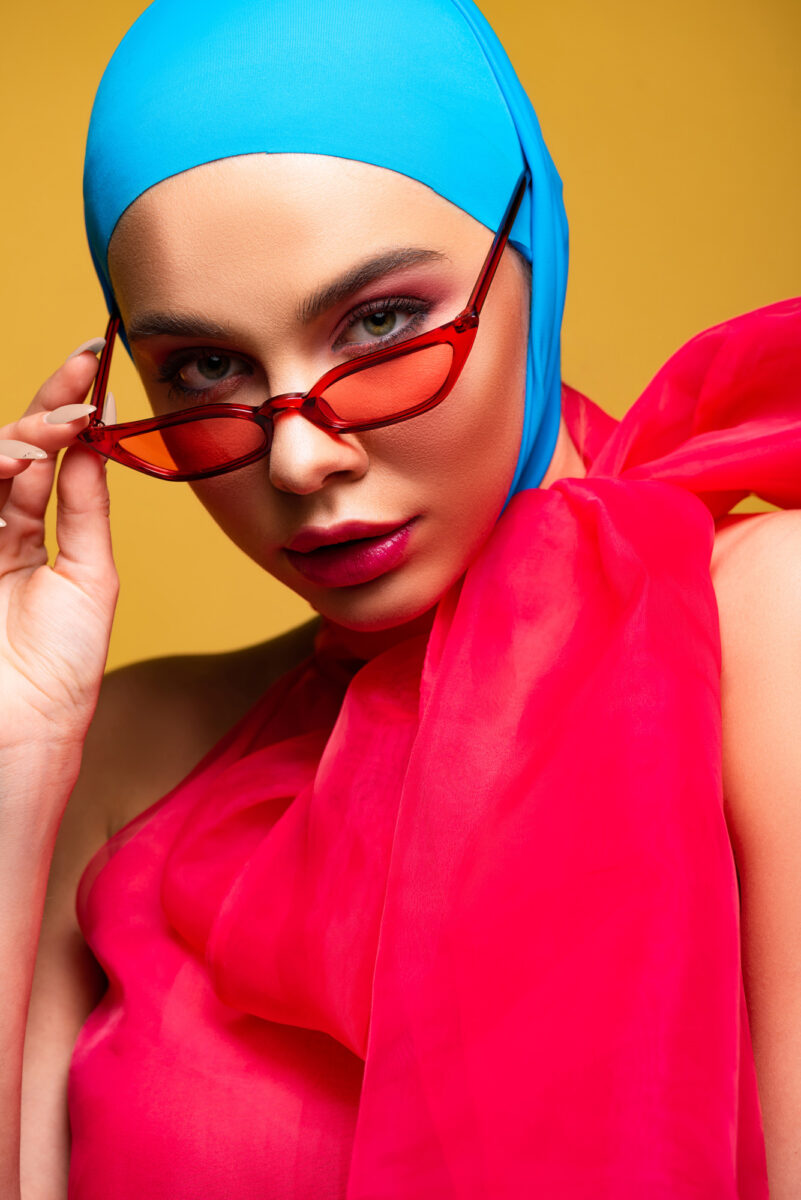A beautiful woman with a vibrant red outfit and blue headgear, set against a contrasting yellow background. The bold and eye-catching colors suggest a lively and energetic theme, reflecting the vibrant hues of the Entity Summer 2024 nail polish collection.