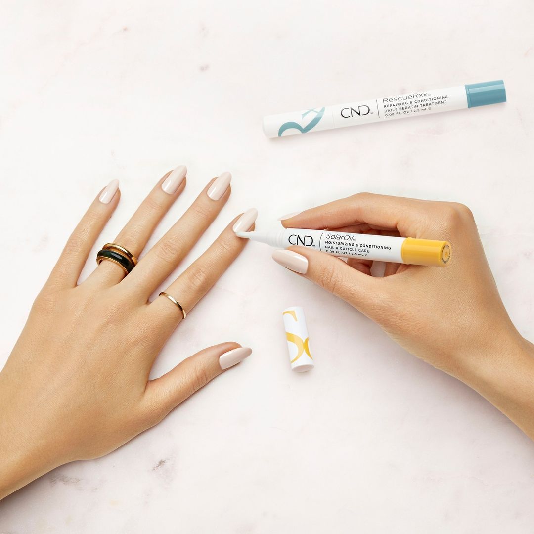 A faceless woman's hand applies CND SolarOil to her nails.