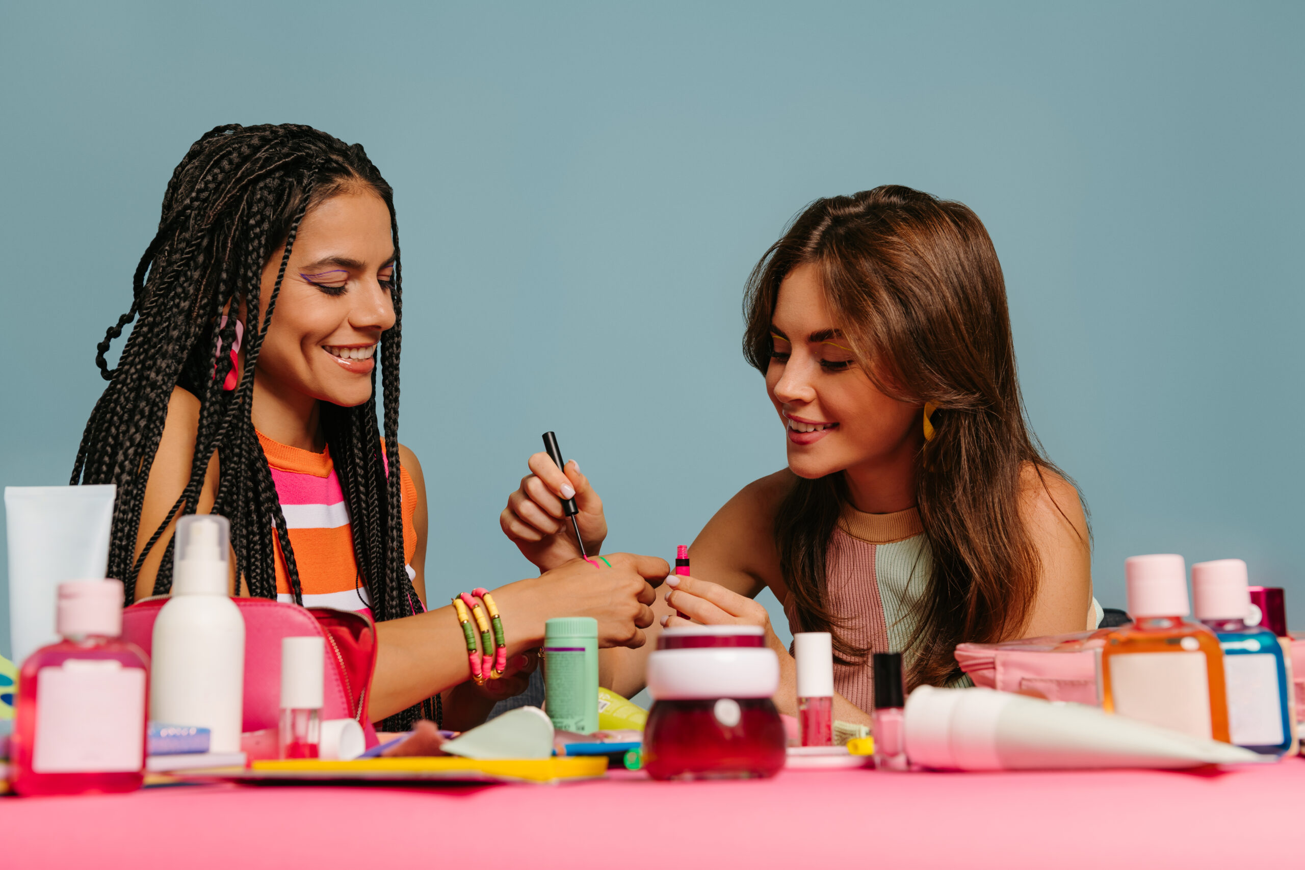 Two happy female presenters testing various beauty products while sitting at the desk on blue background. 2024 nail trends. nail innovations. new nail products.