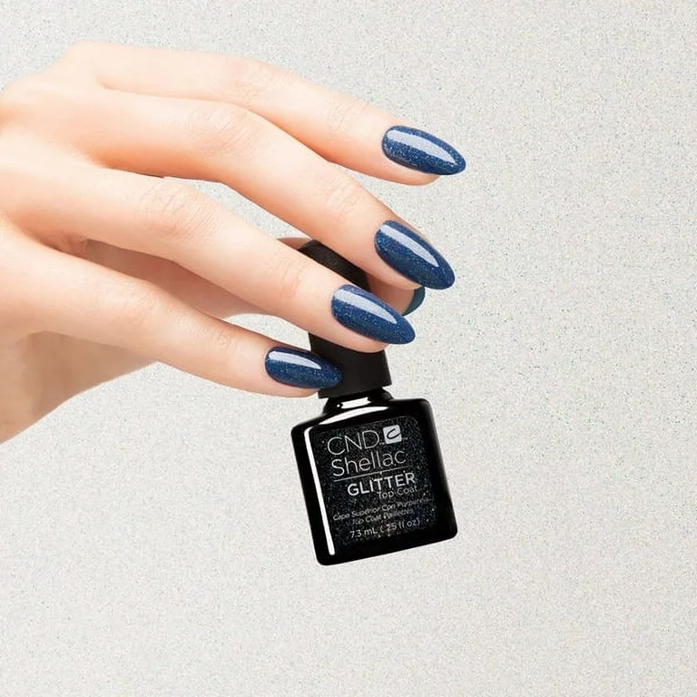 A faceless woman holding a CND Shellac Glitter Top Coat bottle, her nails are painted in bold glossy blue nail polish