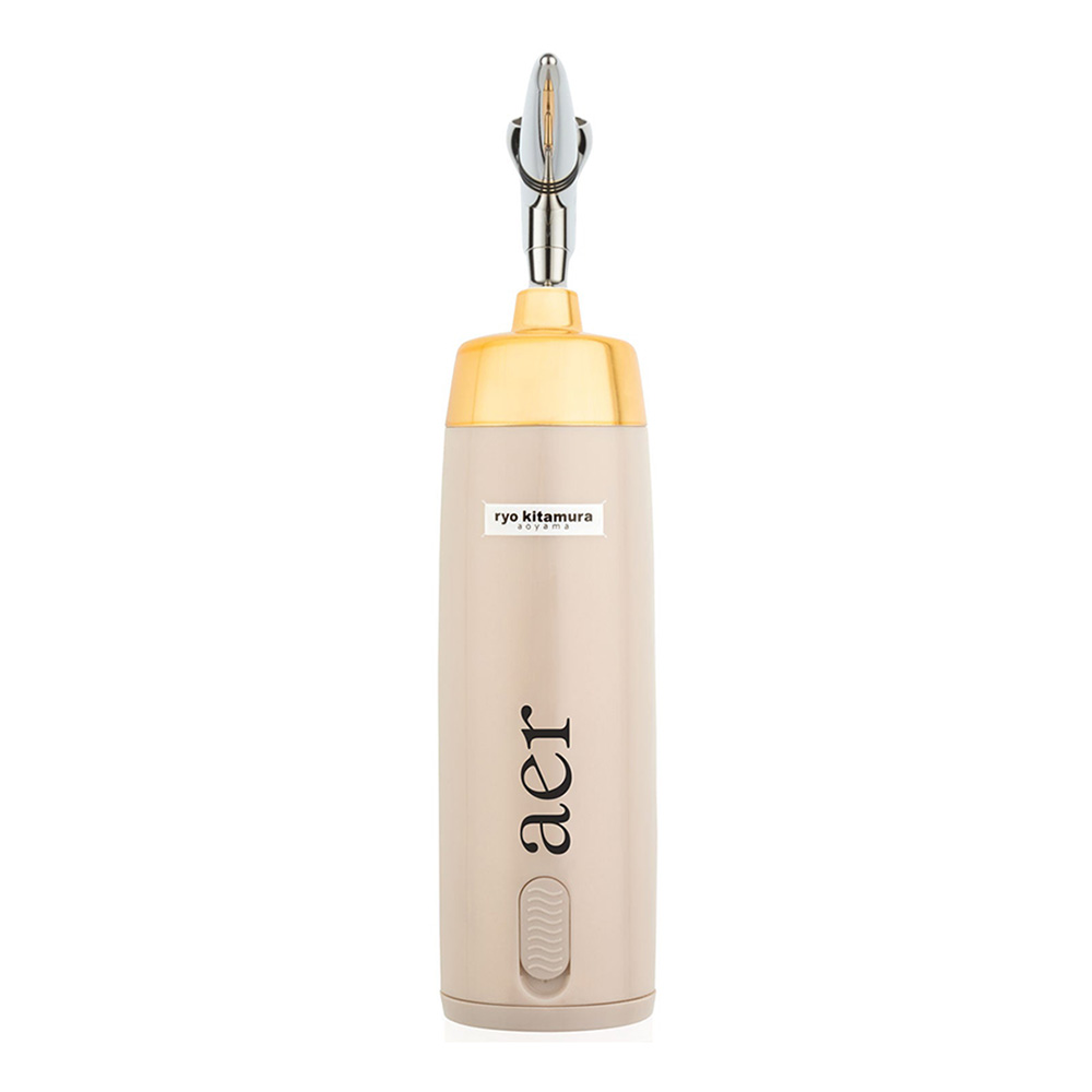 A portable nail drill from the Aprés Nail brand. The drill features a yellow top part and a beige bottom part. It has a silver-colored bit at the top and a keychain loop attached. The beige section displays black text reading ‘ryo kitamura’ above the lowercase brand name ‘aprés.