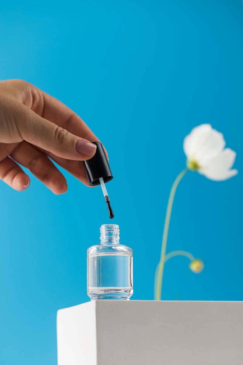 A manicure nail polish bottle. top coat. nail lacquer. blue wall. white flower.