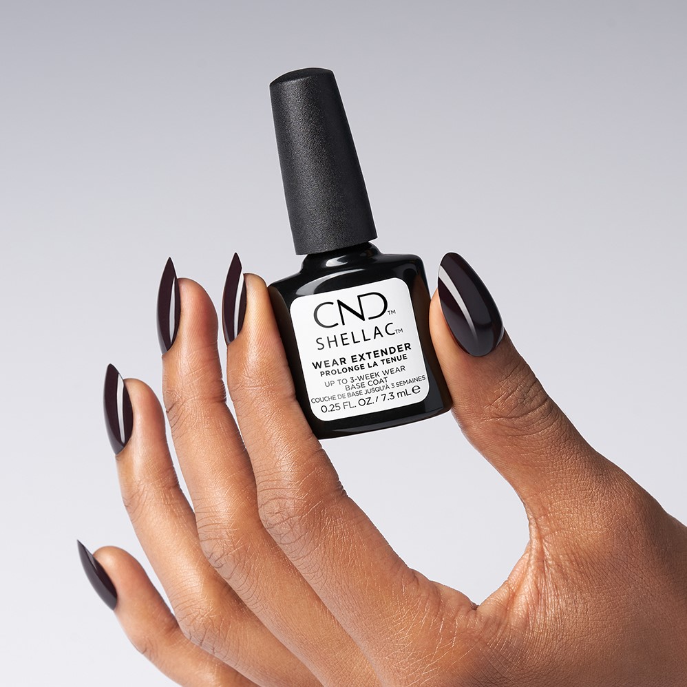 A faceless woman with black painted nails holding the CND SHELLAC wear extended prolonge Tenue base coat. Stain-Blocking Base Coat