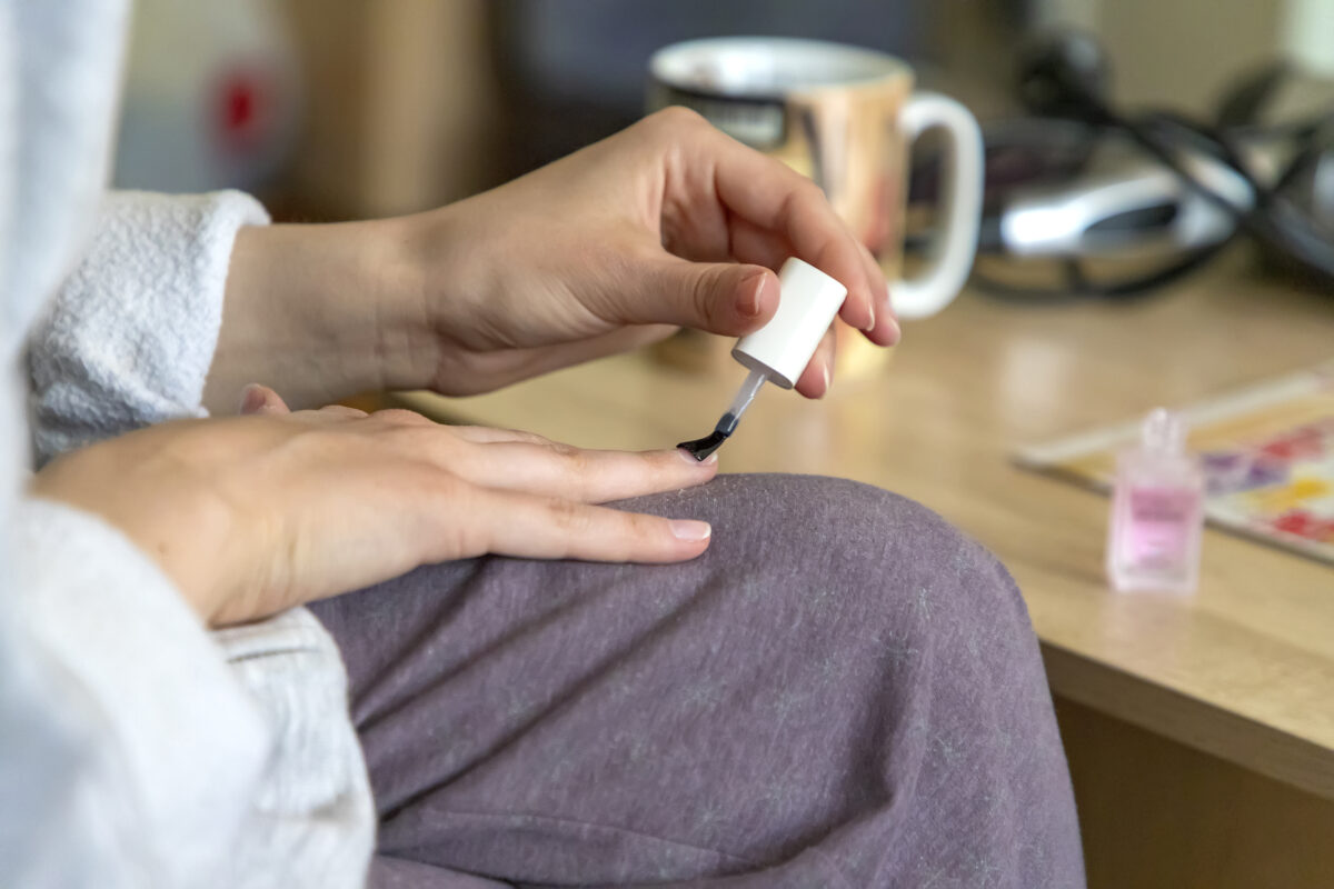A faceless woman applying base coat to her nails. nail care. nail polish. nail lacquer. base gel coat