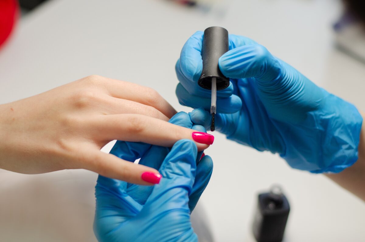 A faceless nail professional applying Strengthening Top Coat to the client's nails