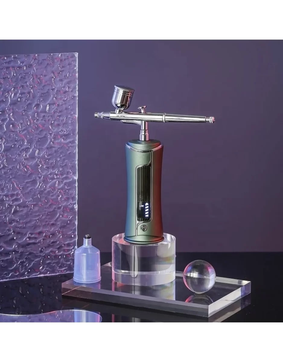 A metallic airbrush, positioned vertically on a clear acrylic stand. Behind the airbrush, there’s a textured glass panel with a purple hue. Two transparent objects are visible before the airbrush: a small bottle containing liquid and a solid sphere, possibly made of glass or acrylic.