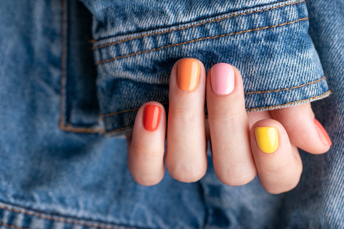 Female hand with colorful manicure on jeans jacket background. gel polish. painted nails.