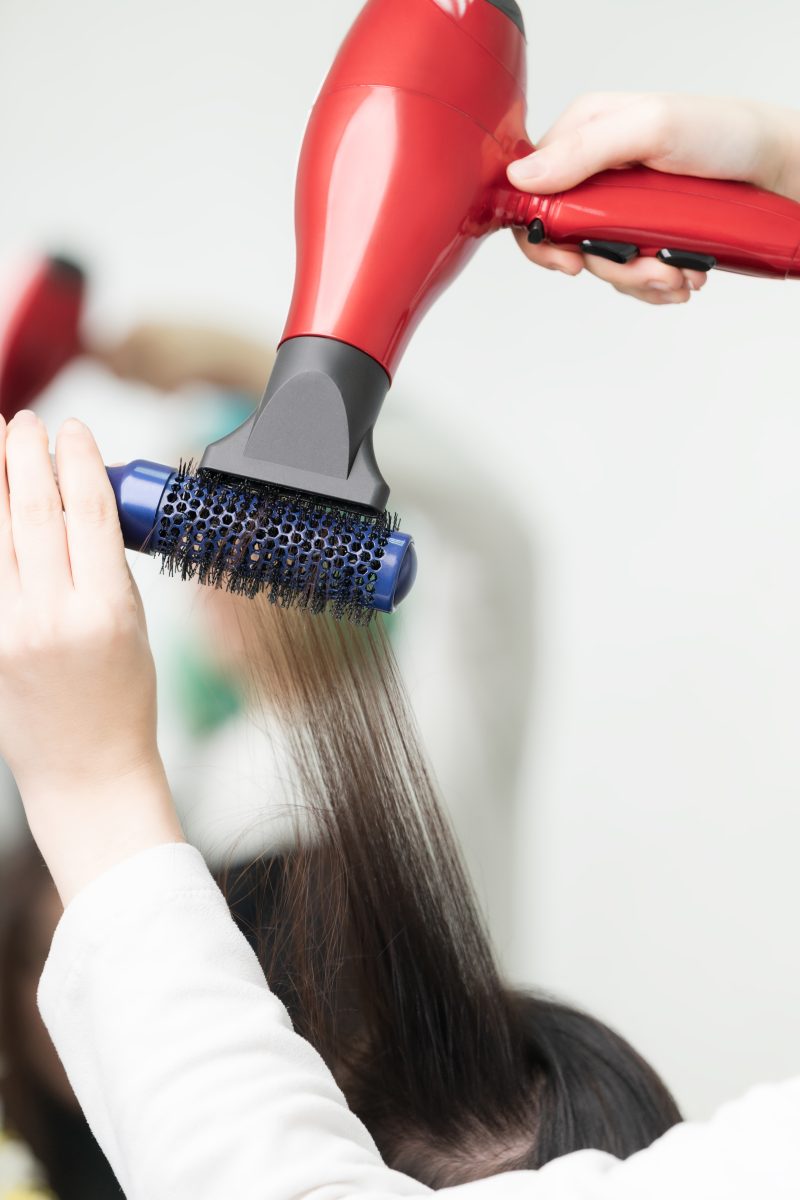  BaBylissPRO Nano Titanium Euphoria Collection. Hands of hairstylist drying brunette hair of client using red hairdryer and blue comb. Occupation in professional beauty salon.
