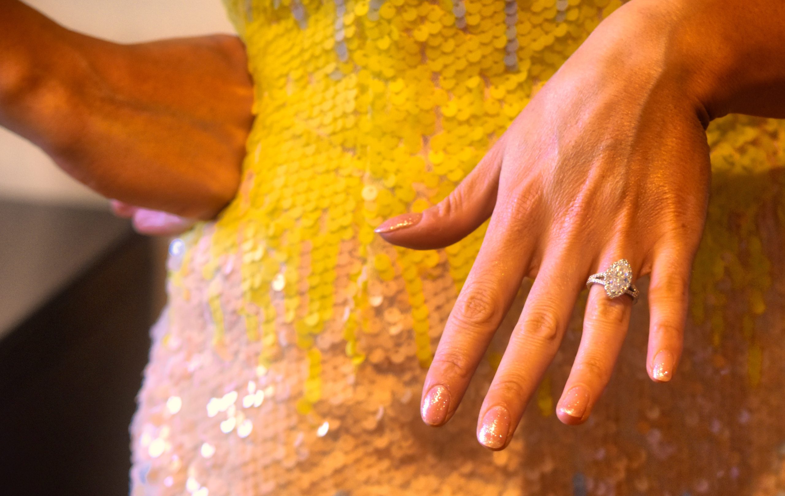 A woman’s hand, featuring a silver engagement ring, with nails painted in light glitter pink polish. CND and celebrities. CND nail polish. CND manicure.