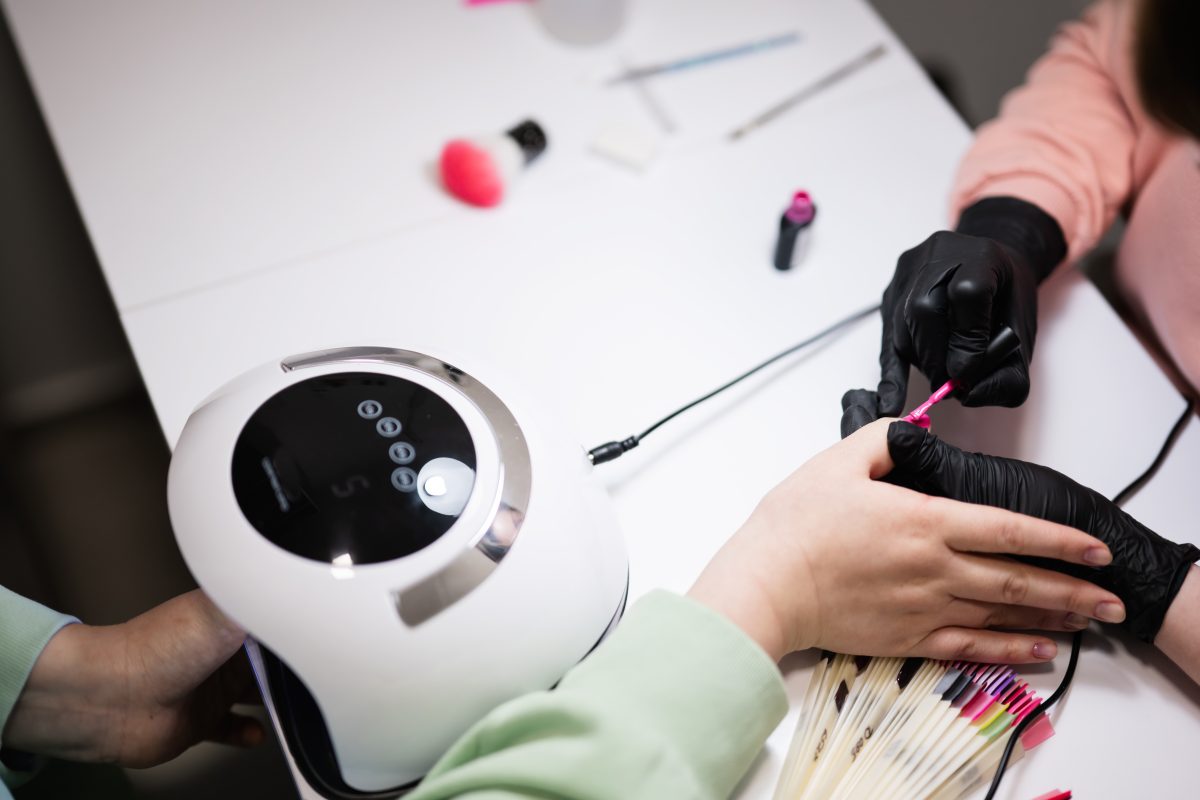 Top view of manicure master working with female client in beauty salon. Manicurist makes woman nail. The best LED lamp released in 2024 for nail salons.