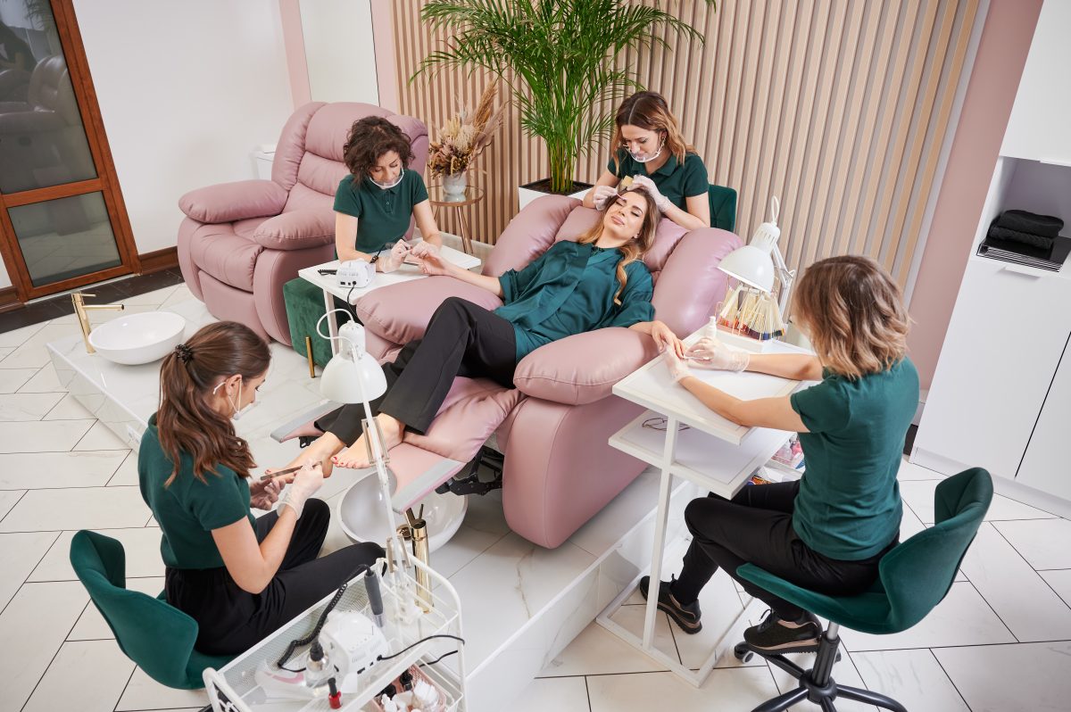 Manicurist, pedicurist and eyelash specialist working with client in modern beauty salon. Woman relaxing in comfortable salon chair while having manicure, pedicure and eyelash extension procedure. Manicure. Pedicure. Nail services.