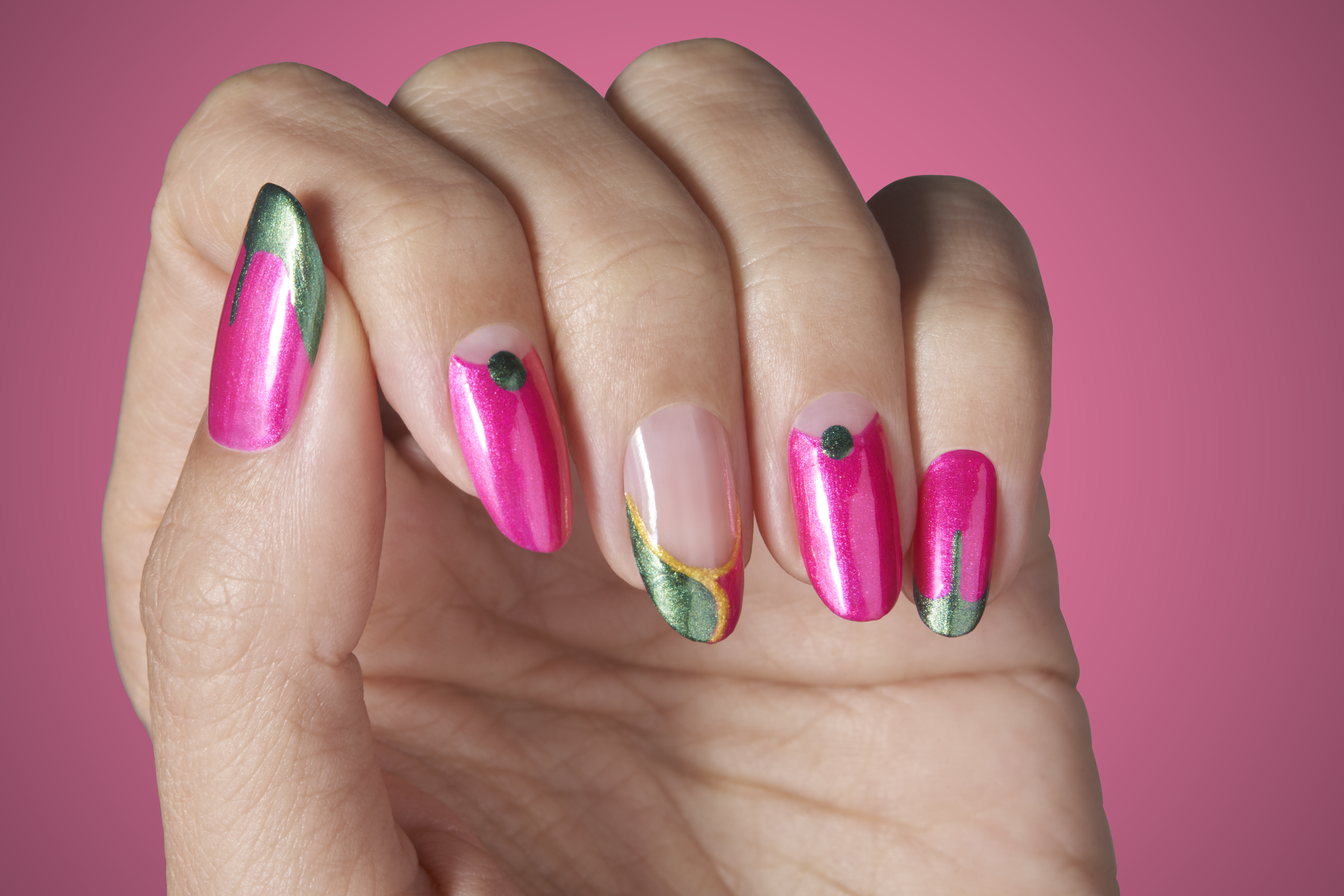A close-up of a hand with a holiday-themed manicure from the OPI Holiday Winter 2024 Nail Polish Collection. The nails are long, stiletto-shaped, and feature shades of pink and green with a metallic sheen. Each nail has a unique design, including solid colors, ombre effects, and decorative accents.