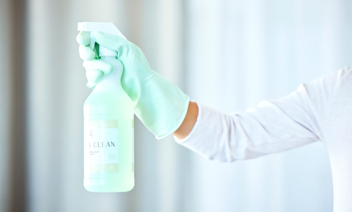 Bottle in hand, arm and spray for cleaning, cleaner and housekeeping with chemical, person with gloves. Spa and salon cleaners. Wax cleaners.