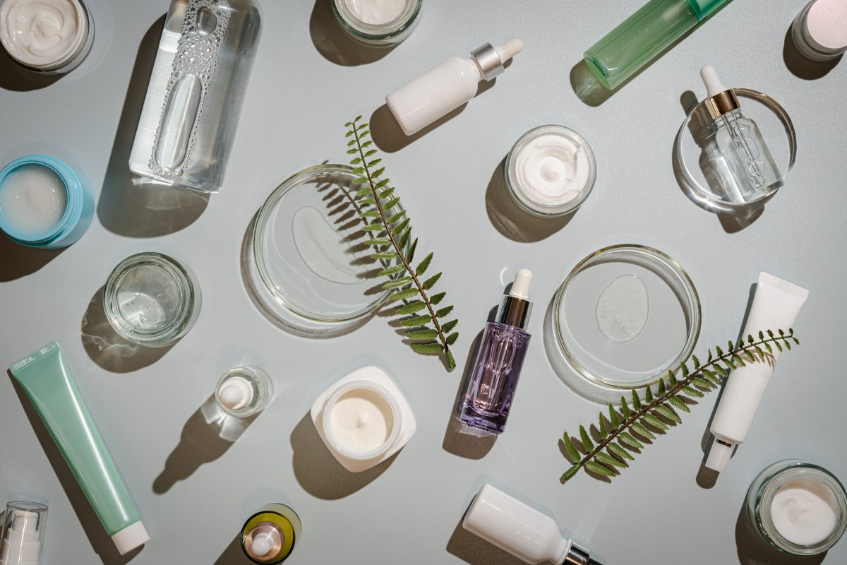 Different glass bottles with serum or oil and cosmetic skin care cream on gray background. Trending shadow. Cosmetic mockup. Top view with copy space. Flat lay. 