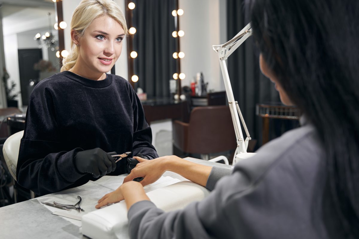 Caucasian female manicurist with scissors in hand while drying painful skin cuticle in beauty center. Freelance Nail Technician.