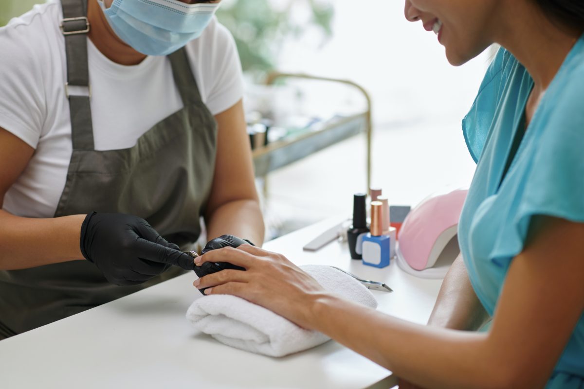 Close-up view of nail technician wearing mask and gloves providing manicure service to customer at nail salon, highlighting hygiene and precision Mobile nail work.