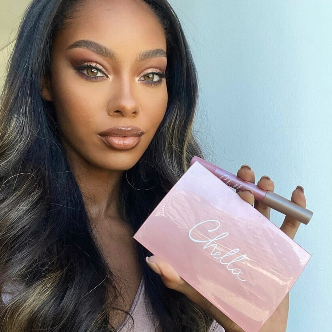 A beautiful woman wearing makeup from Chella Beauty, holding an eyeshadow palette while highlighting her cheekbones, upper lip, tip of her nose, and brow bone with Highlighter Pencils.