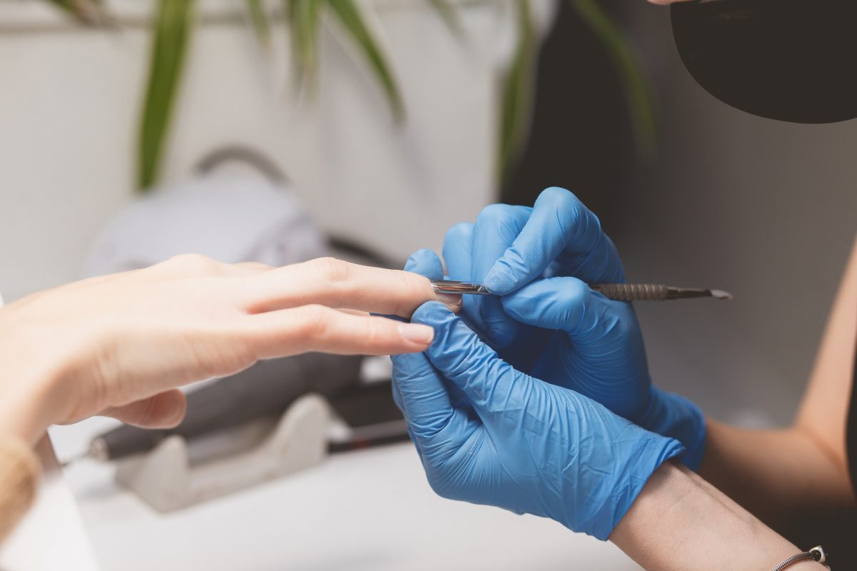 Manicurist cuts cuticle to prepare nails for painting. Manicure procedure closeup.