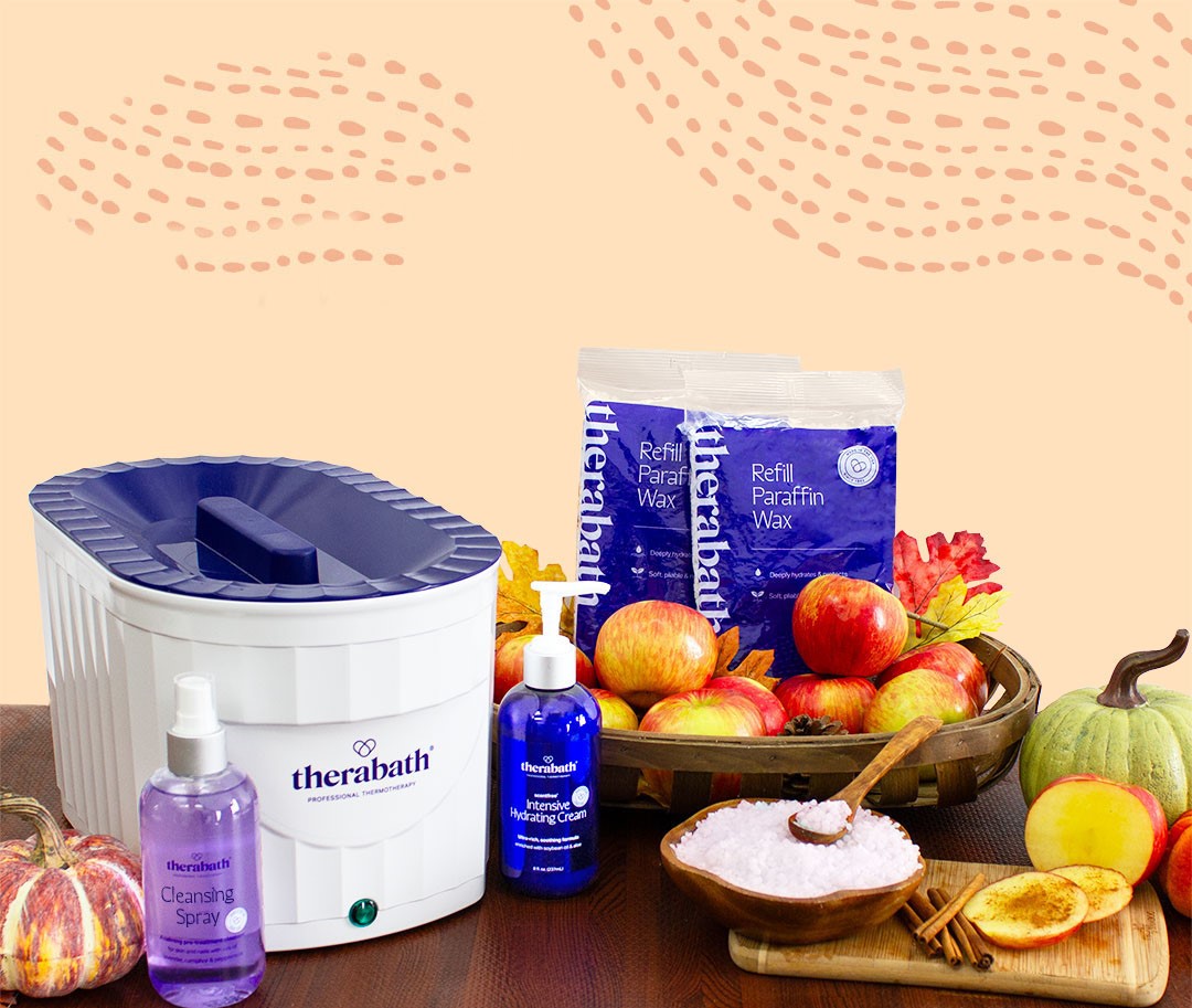 Therabath products displayed with a cozy fall ambiance, including refill paraffin wax, paraffin bath unit, intense hydration cream, and cleansing spray, set among autumn apples, colorful fall leaves, and seasonal fruits.