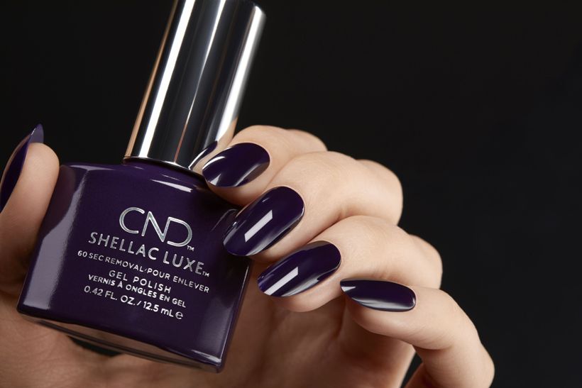 Faceless woman holding a CND SHELLAC Luxe Gel Nail Polish bottle, with nails painted in the matching shade.
