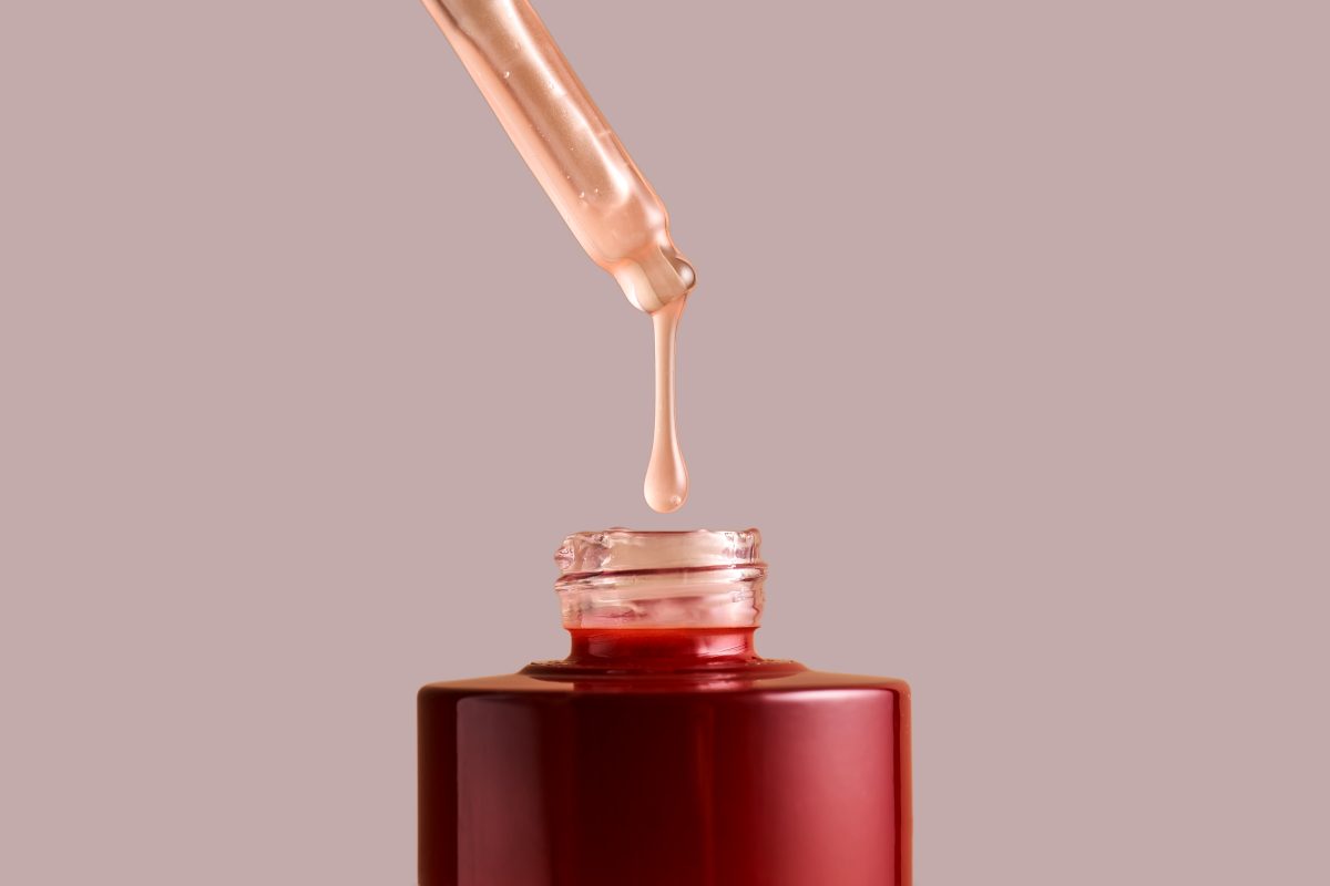 Nail Polish Thinner. A drop of nail polish thinner drips from the dropper into a burgundy nail polish bottle.