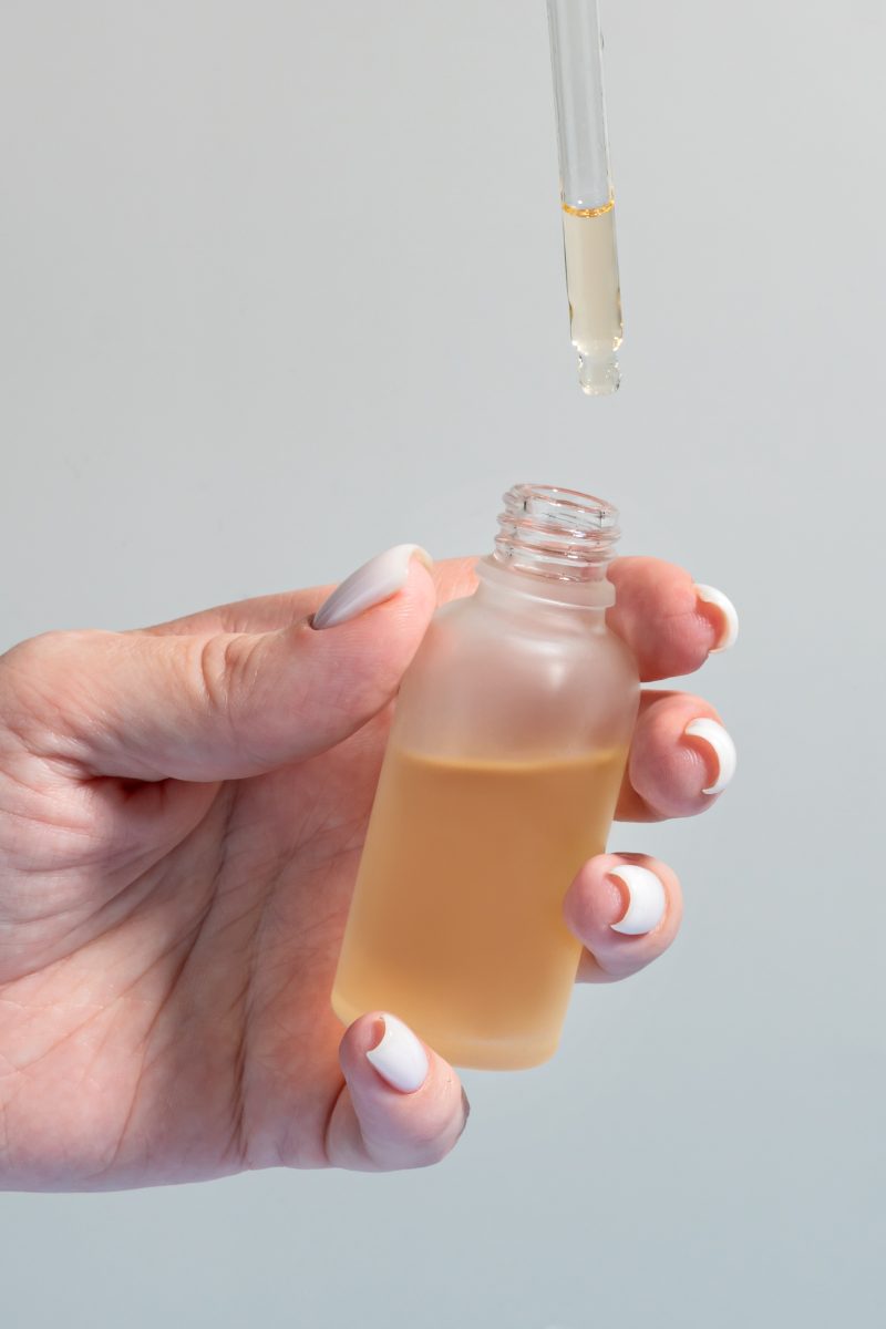 Hand of woman with pipette drop of serum with retinol on light background. Skin care treatment for aged skin. nail polish tools. nail polish thinners. 