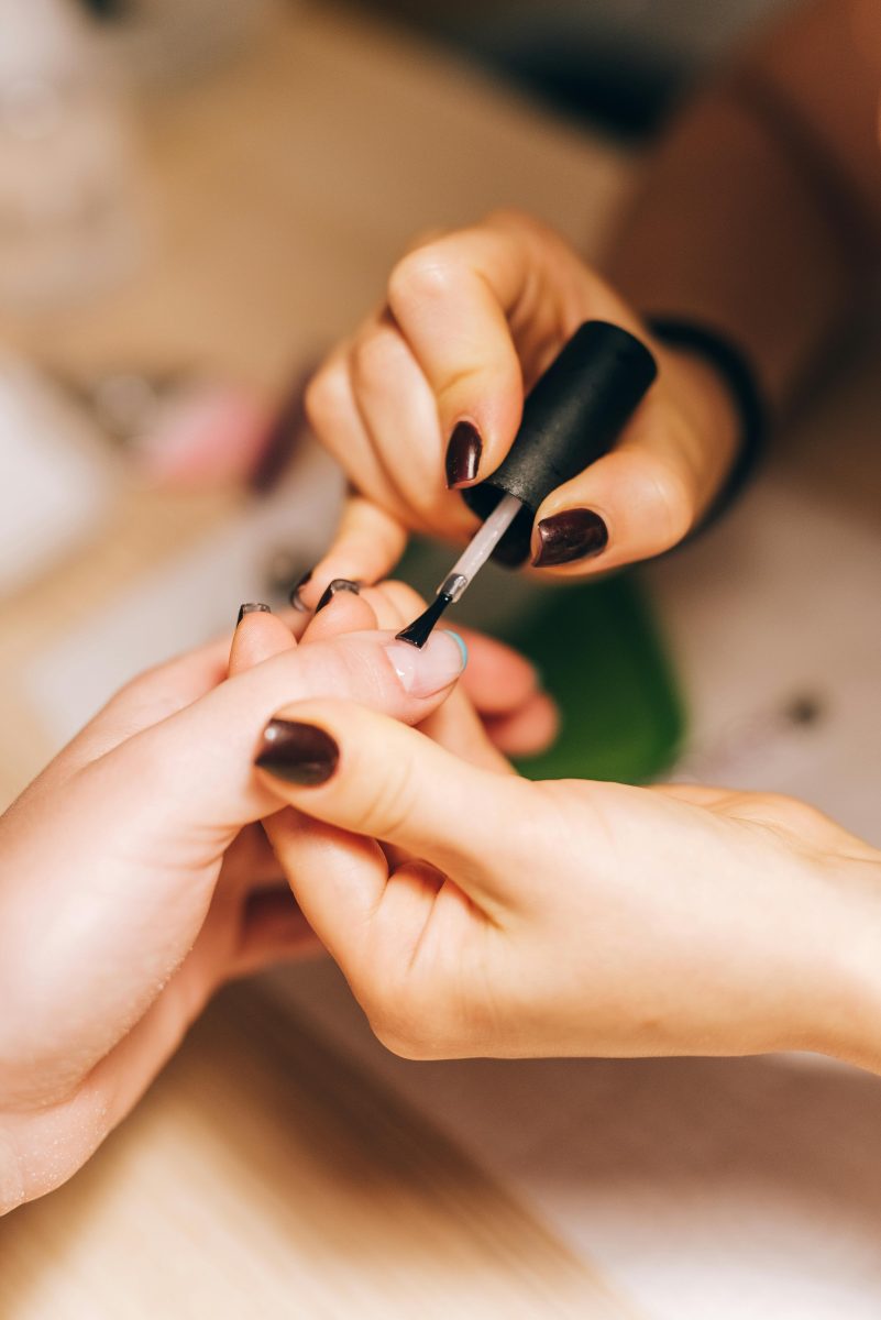 Nail Bonding Products. A faceless nail technician in a salon applying nail glue to a client's nails before attaching nail tips.