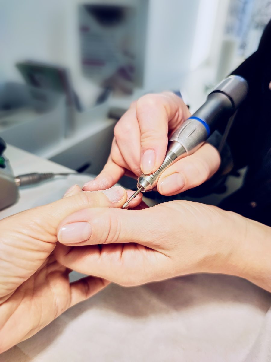Closeup of a woman's hands in a nail salon getting a manicure from a cosmetologist. Manicure machine. A woman does a manicure on her nails. The cosmetologist files the client's nails.