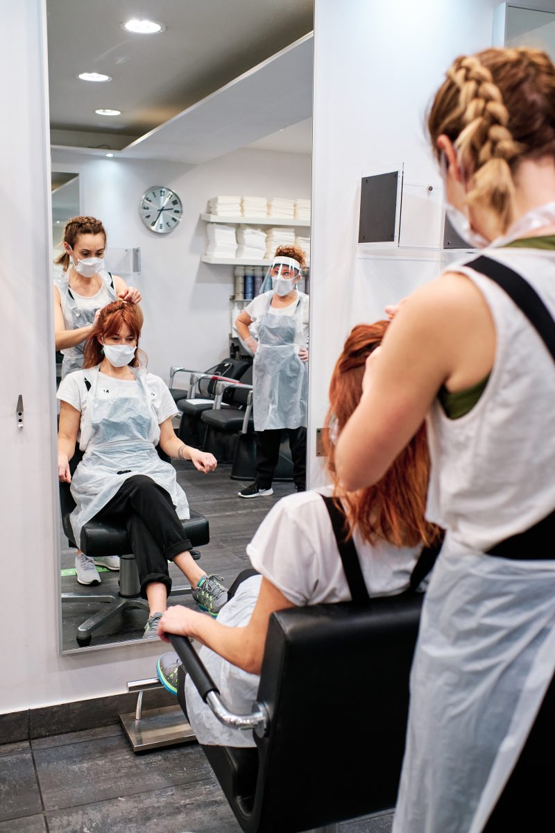 hairdresser in beauty salon with face mask to protect from coronavirus epidemic - social distancing concept. Beauty Schools in Canada