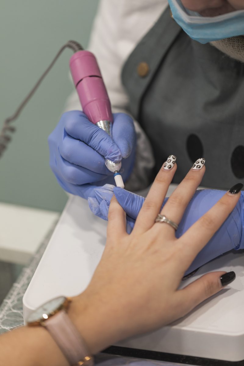 Nail stylist decorating customer's fingernails using nail drill (e-file). Corded vs. Cordless Nail Drills.