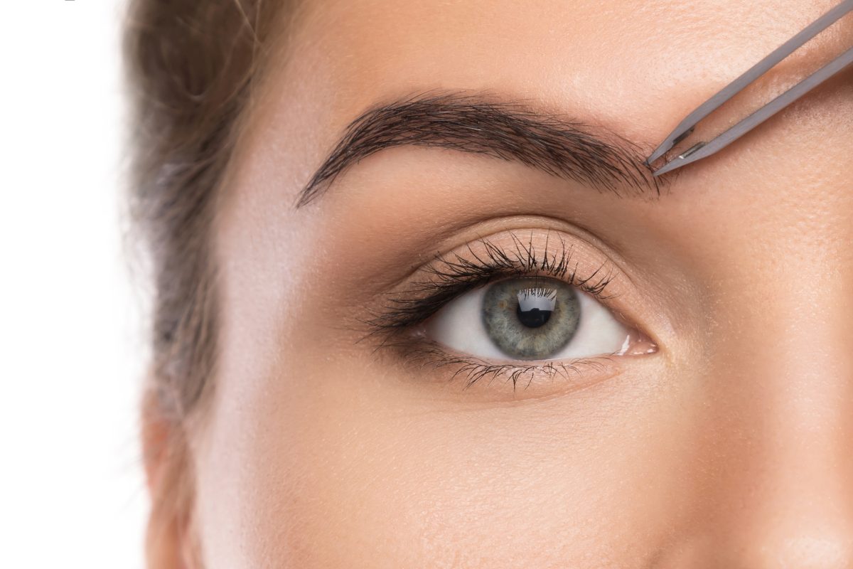 Close up of female face and eyebrow with tweezers