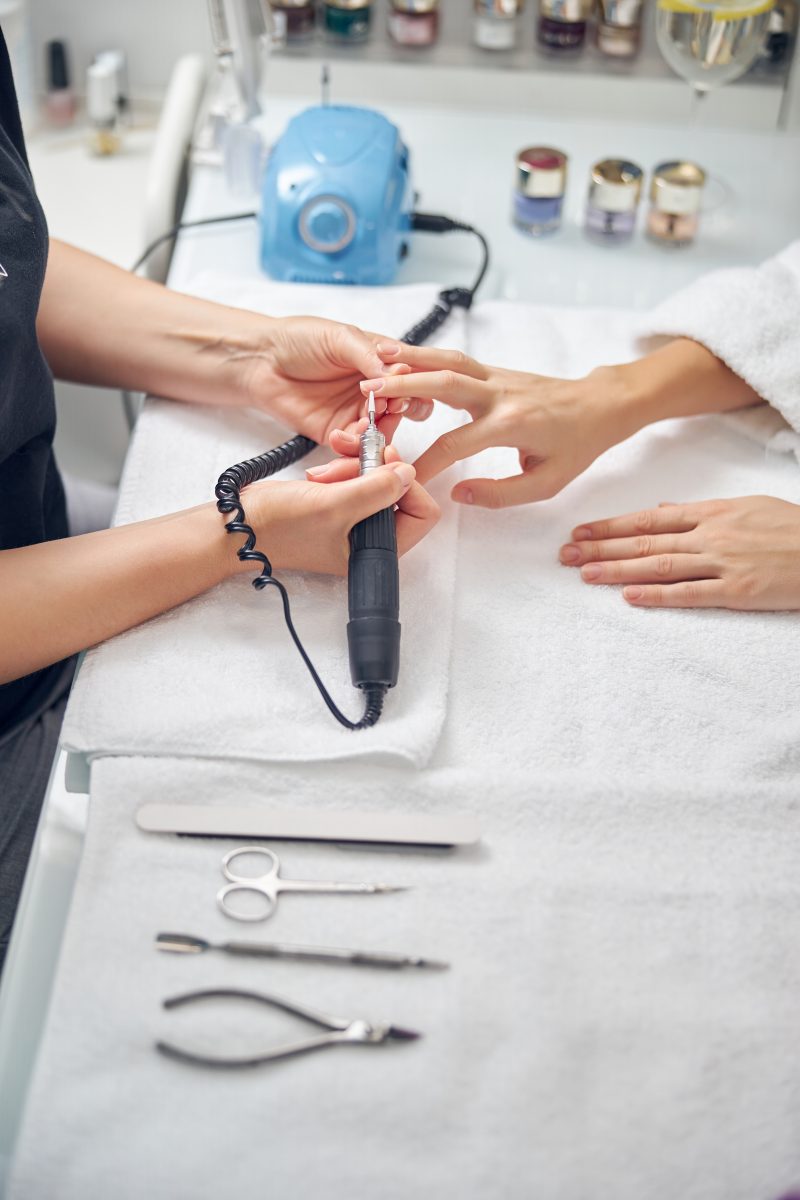 Top view close up of female hands near instruments during procedure of hardware manicure in salon.