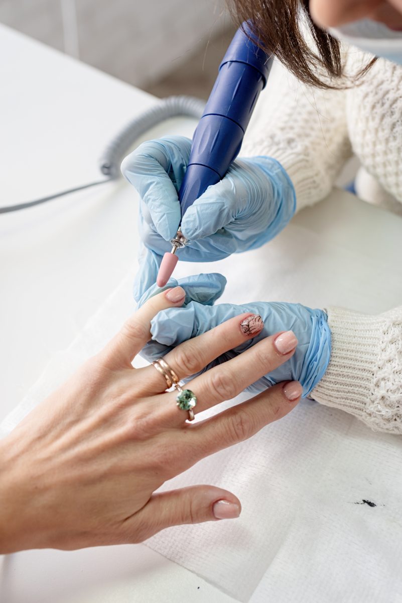 nails master in protective gloves making a manicure to client nails in a nail salon.