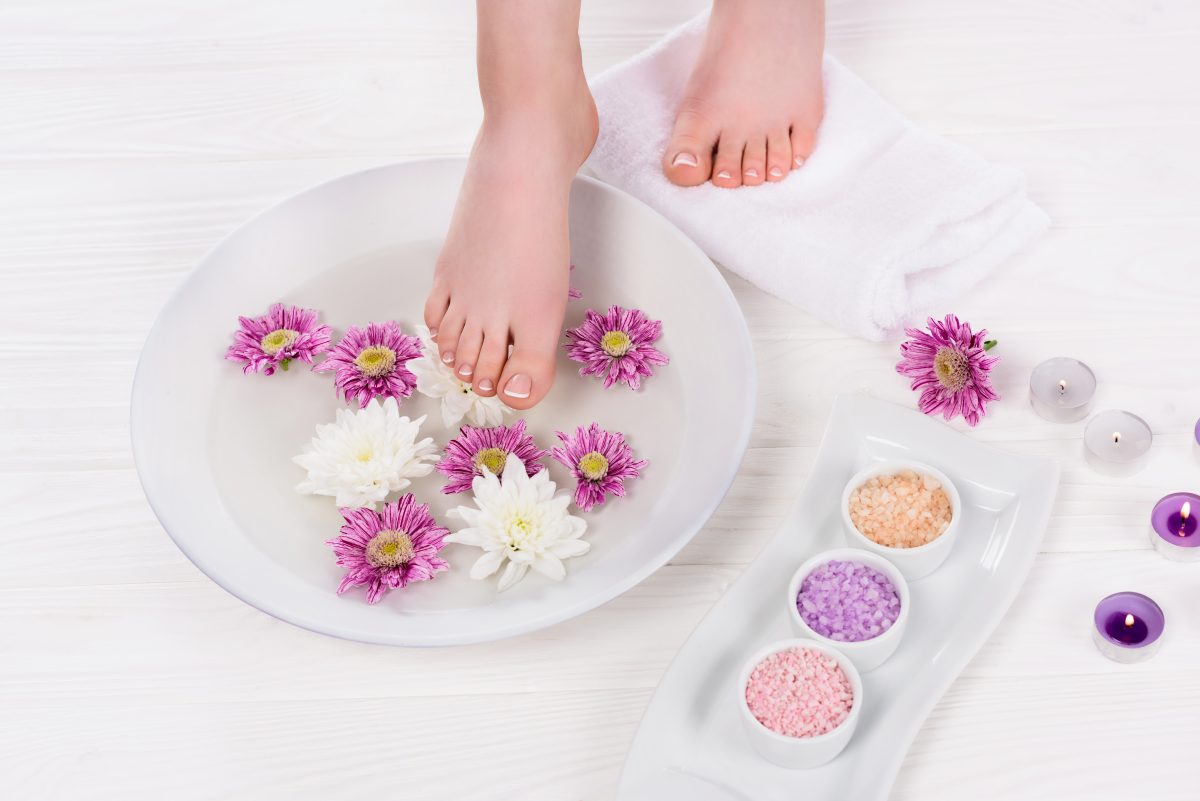 cropped shot of barefoot woman receiving bath for nails with colorful sea salt and flowers near