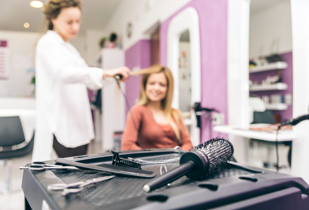 Hair stylist straightening hair to her customer in a modern hairdresser salon, closeup on brushes and scissors
