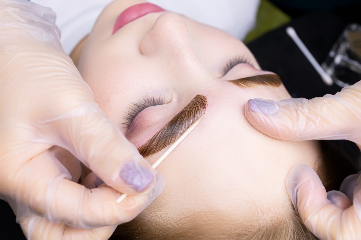macro photography of the model's eyebrows painted and applied eyebrow paint on them, the master tries to remove excess paint from the contour of the eyebrows with a cotton swab