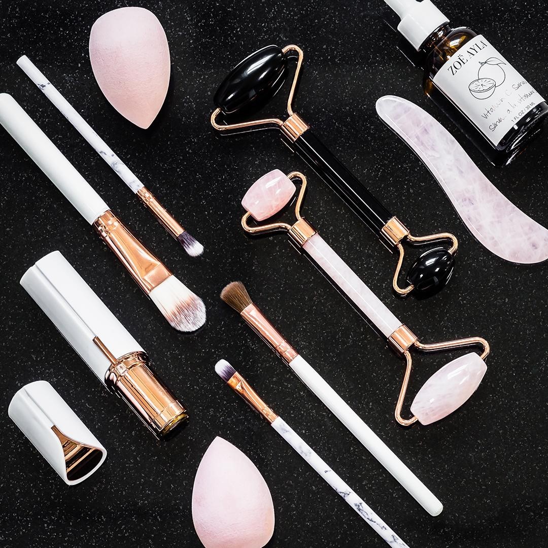 A curated collection of Zoë Ayla beauty and skincare products displayed on a sleek surface. The arrangement features tools such as facial rollers, Gua Sha tools, makeup brushes, and skincare bottles, showcasing the brand's modern, elegant designs and high-quality materials. The vibrant colors and sophisticated presentation emphasize the blend of luxury and functionality that Zoë Ayla is known for.