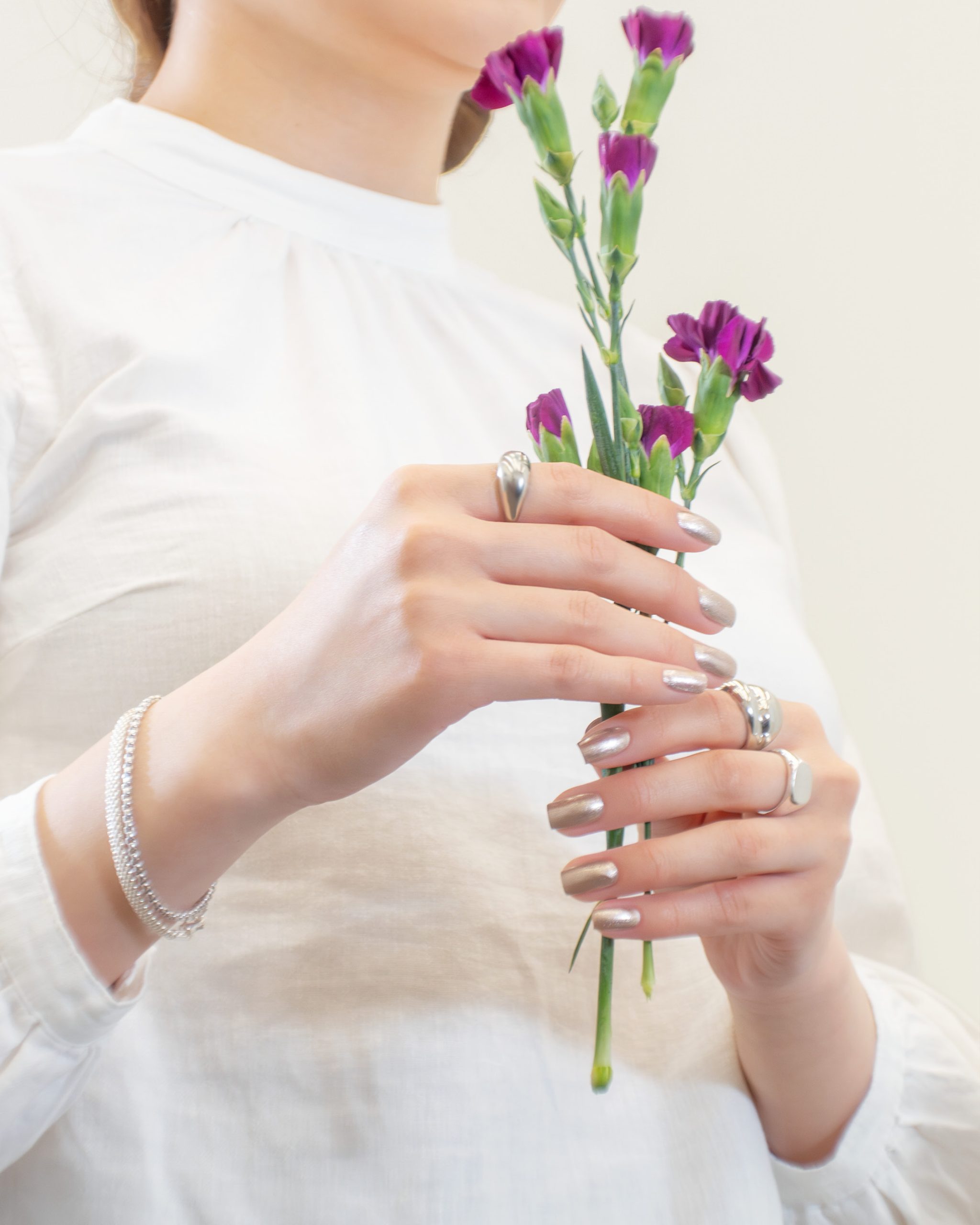 A close-up of elegantly manicured hands holding fresh purple flowers, showcasing a natural, glossy nail look with Morgan Taylor Naturals polish.