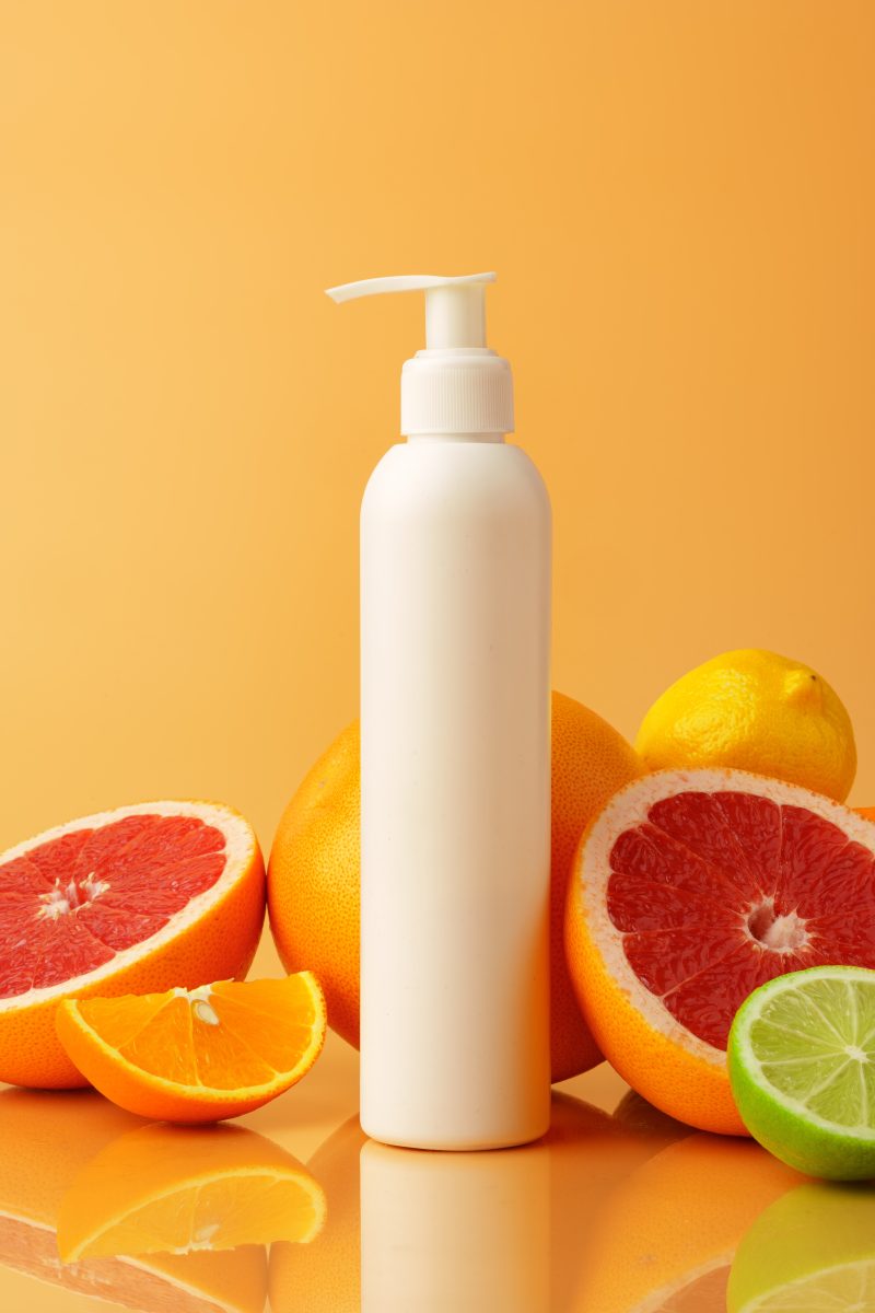 Cosmetic container on orange background with cut citrus fruit. Body Lotion Brands.