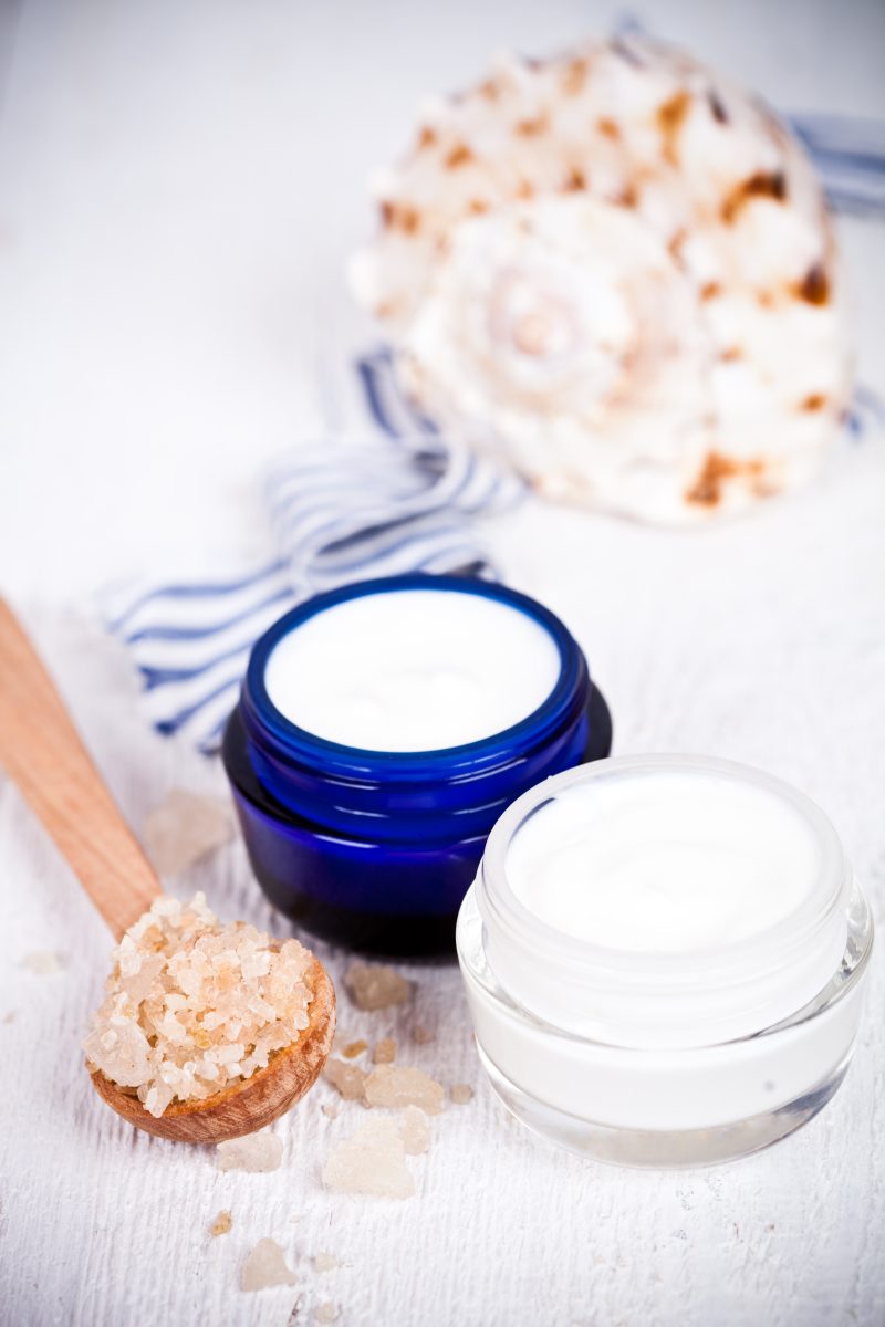 face cream in jars with sea salt and shell closeup. Popular Brands of Body Butters and Lotions.