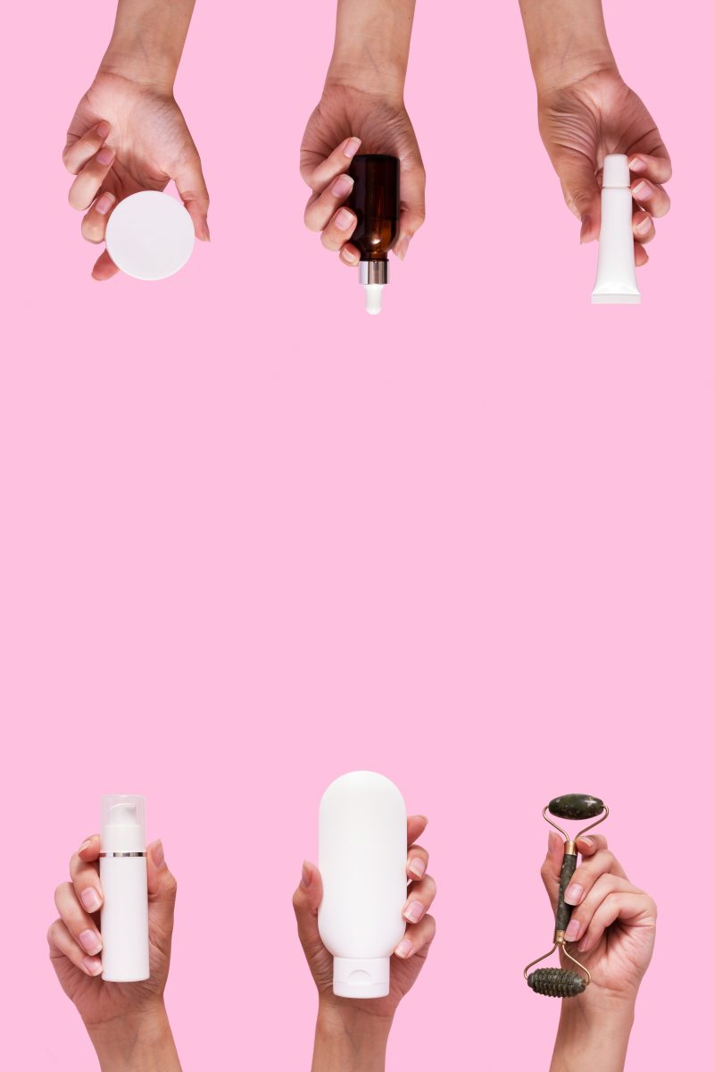 Types of Pre-Wax Products & Their Benefits. Female hands with cosmetic products in different containers and bottles mock up isolated on pink color background. Vertical format..