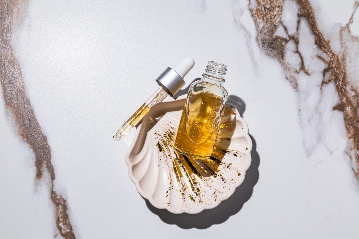 Dry Body Oil Ingredients to Look for. An open bottle of serum and a pipette filled with a cosmetic product. Hyaluronic acid, panthenol, gold 24k. Abstract marble background. rejuvenation