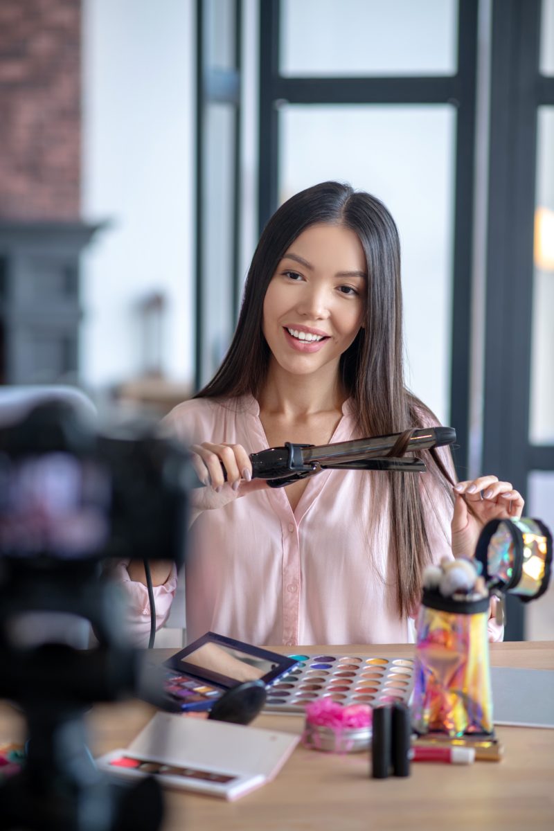 Woman doing hairstyle. Appealing dark-eyed woman doing hairstyle in front of camera while making new blog