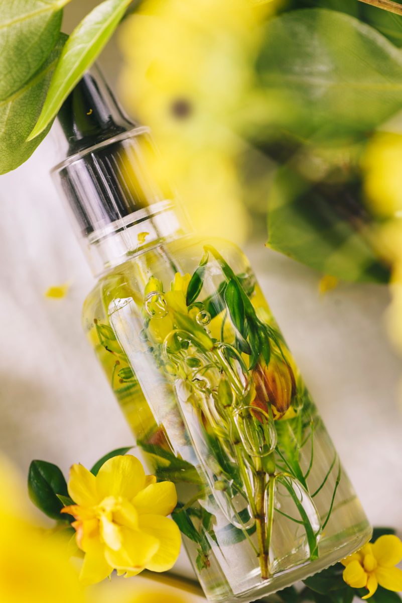 Detail essential oil of almonds, with flowers and natural herbs, on a background of green leaves.